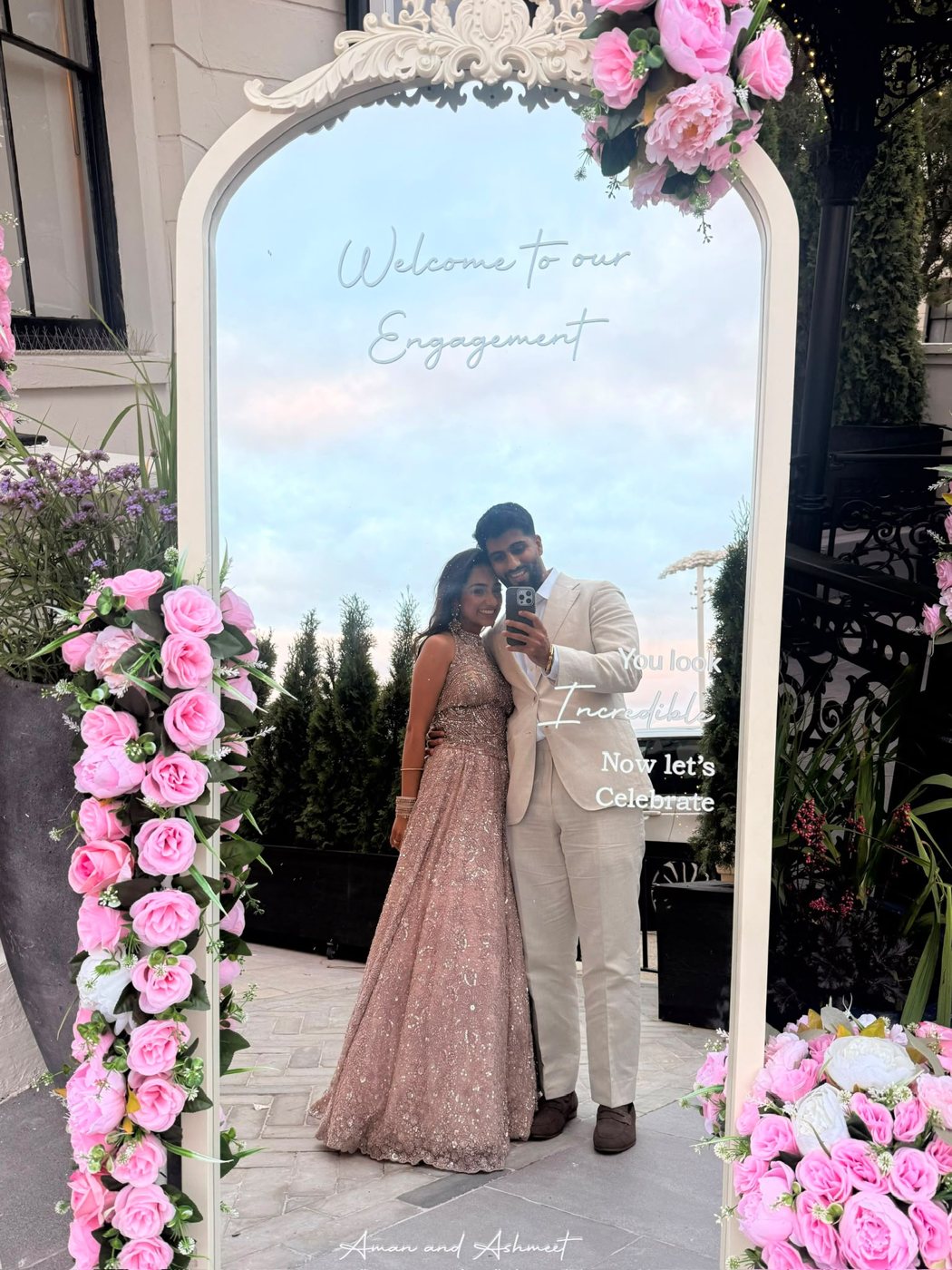 Aman and Ashmeet taking a mirror selfie at their engagement party, framed by pink roses